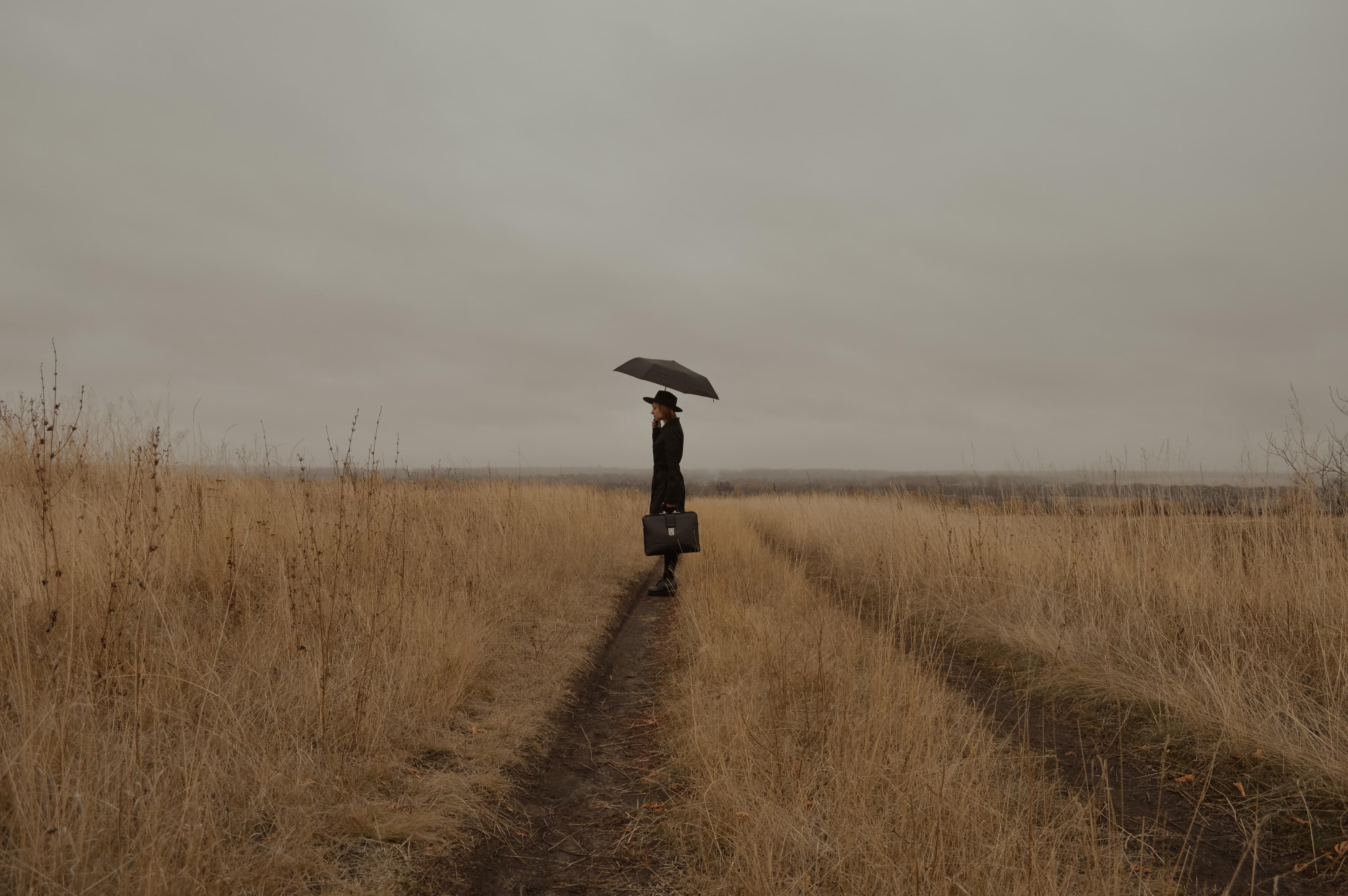 Woman standing alone in field with umbrella up